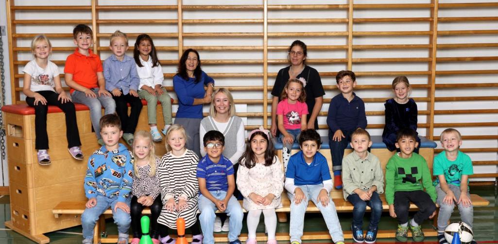 1a sitzt auf Langbänken und Kästen mit buntem Spielmaterial im Turnsaal.