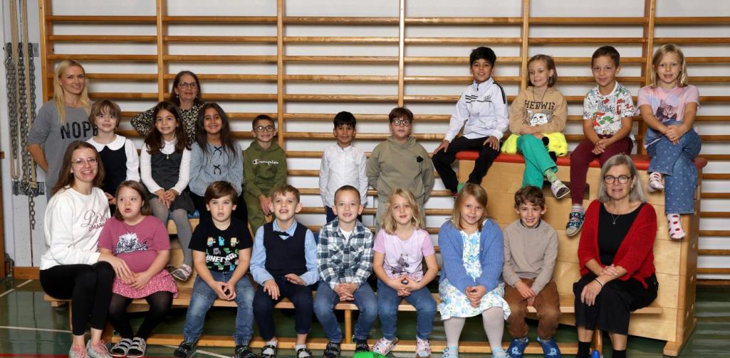 2a sitzt auf Langbänken und Kästen mit buntem Spielmaterial im Turnsaal.