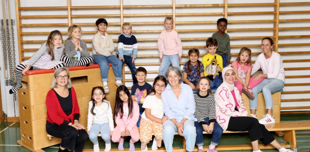 2b sitzt auf Langbänken und Kästen mit buntem Spielmaterial im Turnsaal.