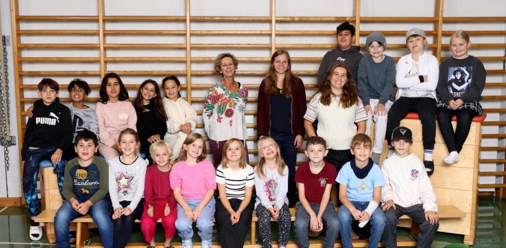 3b sitzt auf Langbänken und Kästen mit buntem Spielmaterial im Turnsaal.