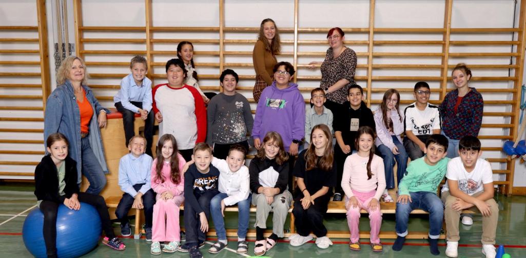 4b sitzt auf Langbänken und Kästen mit buntem Spielmaterial im Turnsaal.