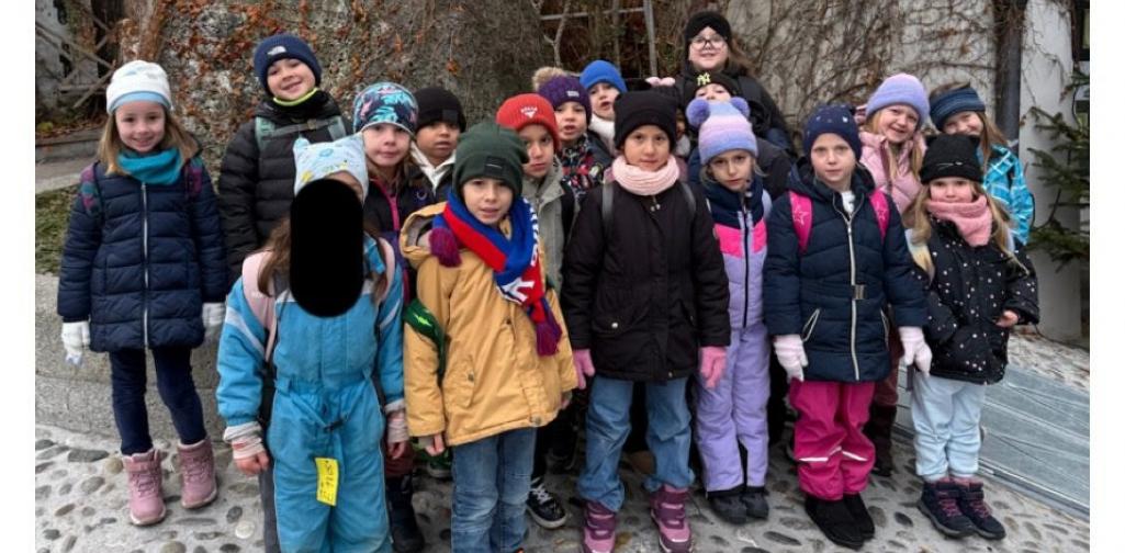 Alexandra Sigitz Eine Gruppe von Kindern in winterlicher Kleidung steht dicht zusammen für ein Gruppenfoto vor einer Statue und einer mit Efeu bewachsenen Wand. Ein Kind ist im Gesicht aus Datenschutzgründen geschwärzt.