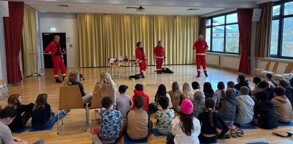 Rettungshundeführerinnen und -führer stellen ihre Ausrüstung vor und erklären den Kindern in der Aula die Arbeit der Rettungshundestaffel.