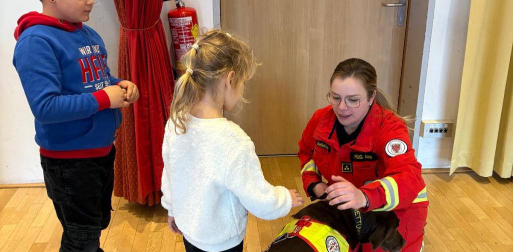 Eine Rettungshundeführerin lässt Kinder einen Rettungshund vorsichtig streicheln und erklärt den richtigen Umgang mit dem Tier.