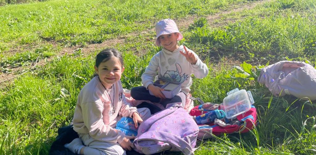 „Zwei Schülerinnen sitzen auf einer Wiese und essen ihre Jause während eines Ausflugs im Freien.“