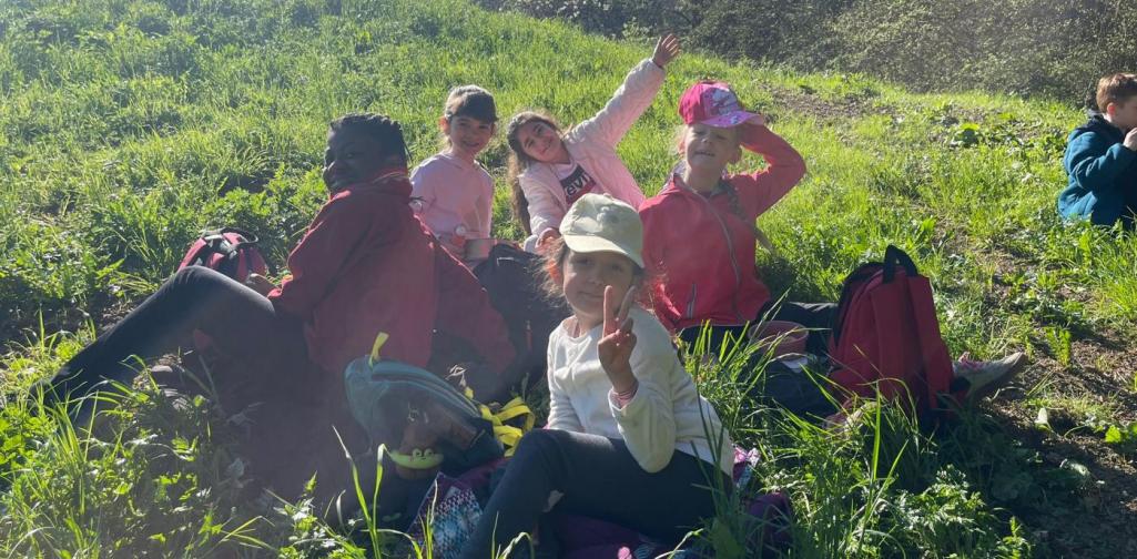 „Mehrere Schüler:innen sitzen gemeinsam auf einer Wiese und machen während eines Ausflugs eine Pause.“