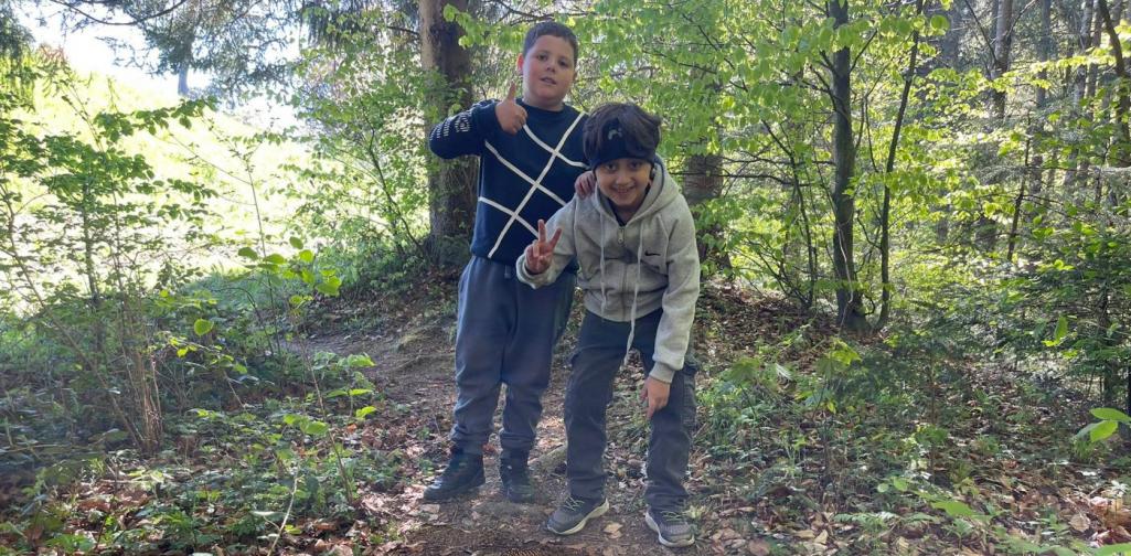 „Zwei Schüler stehen im Wald neben einem Kreis aus Tannenzapfen, den sie auf dem Boden gelegt haben.“