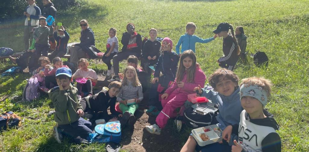 VS Amras Kinder machen während einer Exkursion auf einer Wiese eine gemeinsame Jausenpause im Freien.
