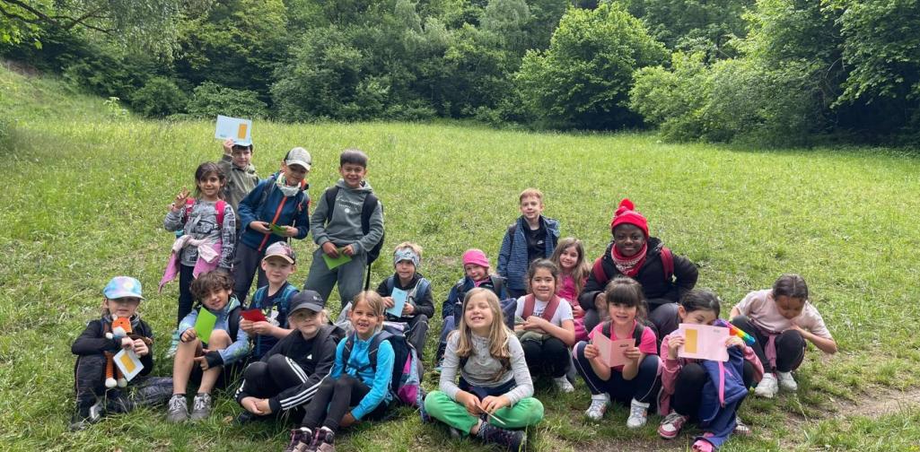 VS Amras Kinder einer Schulklasse bei einer Exkursion auf einer Waldwiese mit Arbeitsmaterialien in den Händen.