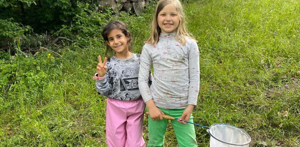 VS Amras Kinder erkunden bei einer Exkursion eine Wiese am Waldrand und halten einen Kescher für Naturbeobachtungen bereit.