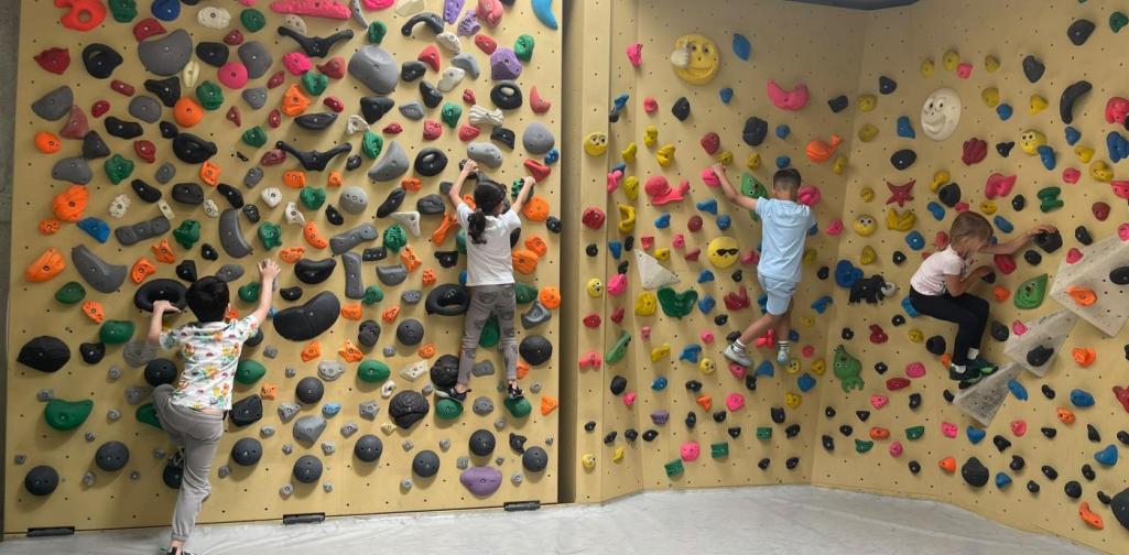 Kinder klettern und bouldern an einer bunten Indoor-Kletterwand mit unterschiedlich schwierigen Routen.
