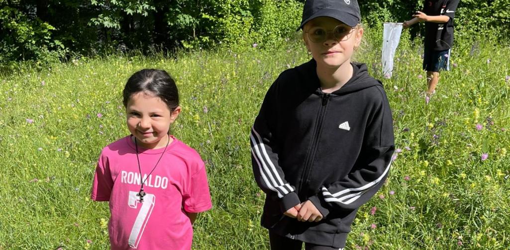 VS Amras Kinder beobachten die Natur auf einer blühenden Wiese während einer Exkursion im Freien.