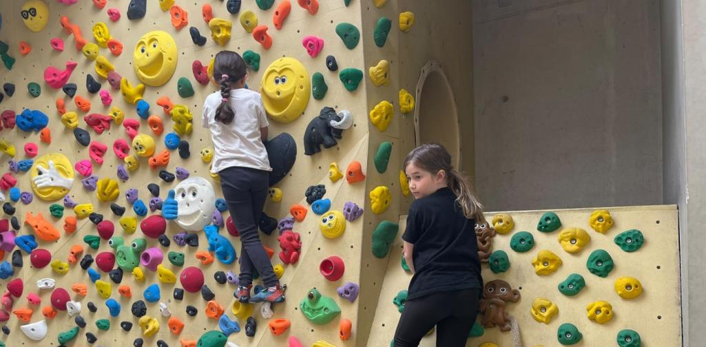 Zwei Kinder bouldern an einer Indoor-Kletterwand mit bunten Griffen und erkunden verschiedene Kletterwege.