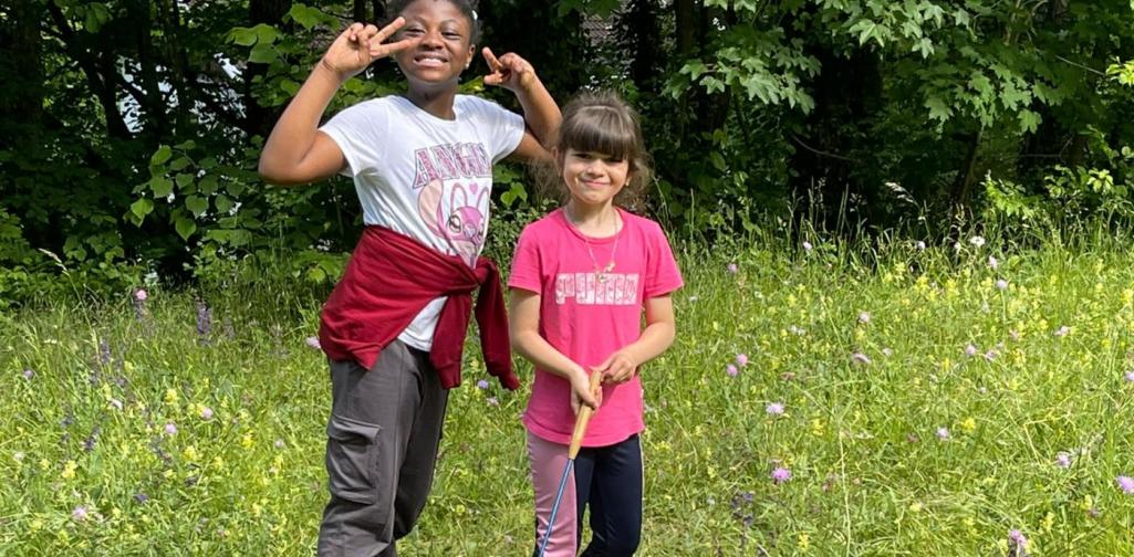 VS Amras Kinder erkunden mit einem Kescher eine blühende Wiese und beobachten die Natur am Waldrand.