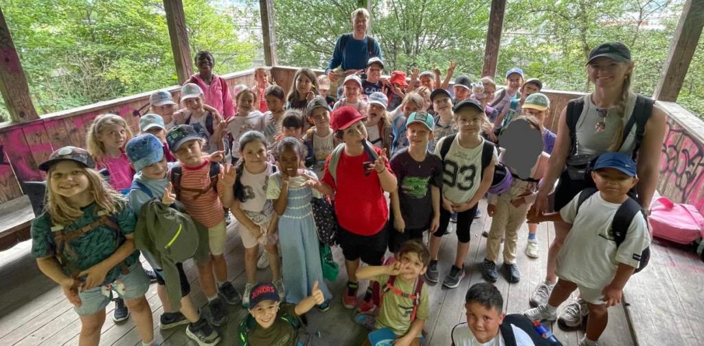 Die Kinder der 1A und 1B machen gemeinsam mit ihren Lehrpersonen ein Gruppenfoto auf einem überdachten Aussichtspunkt.