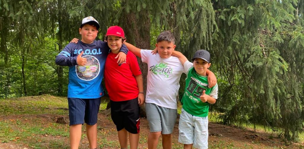 Vier Kinder stehen Arm in Arm vor einem großen Baum im Schlosspark und lächeln in die Kamera.