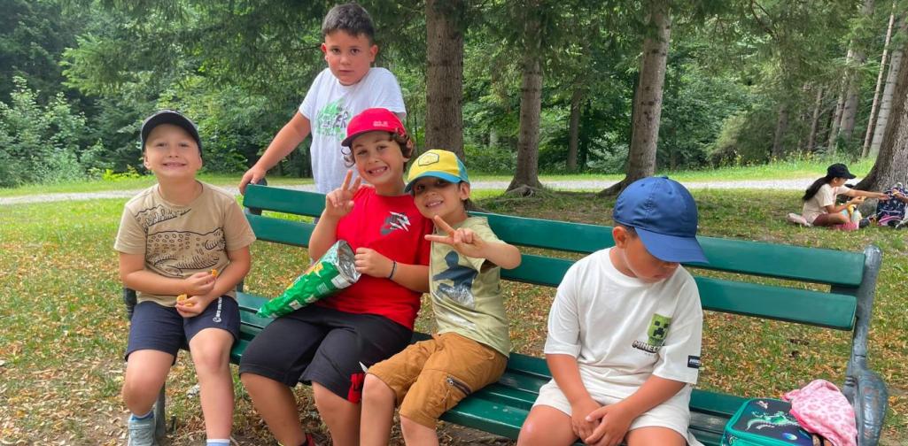 Kinder sitzen gemeinsam auf einer Parkbank im Schlosspark und machen fröhlich eine Pause.“
