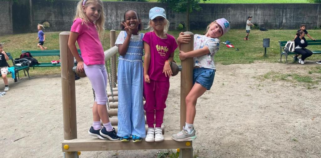 Vier Kinder posieren lächelnd auf einem Klettergerüst am Spielplatz im Schlosspark.
