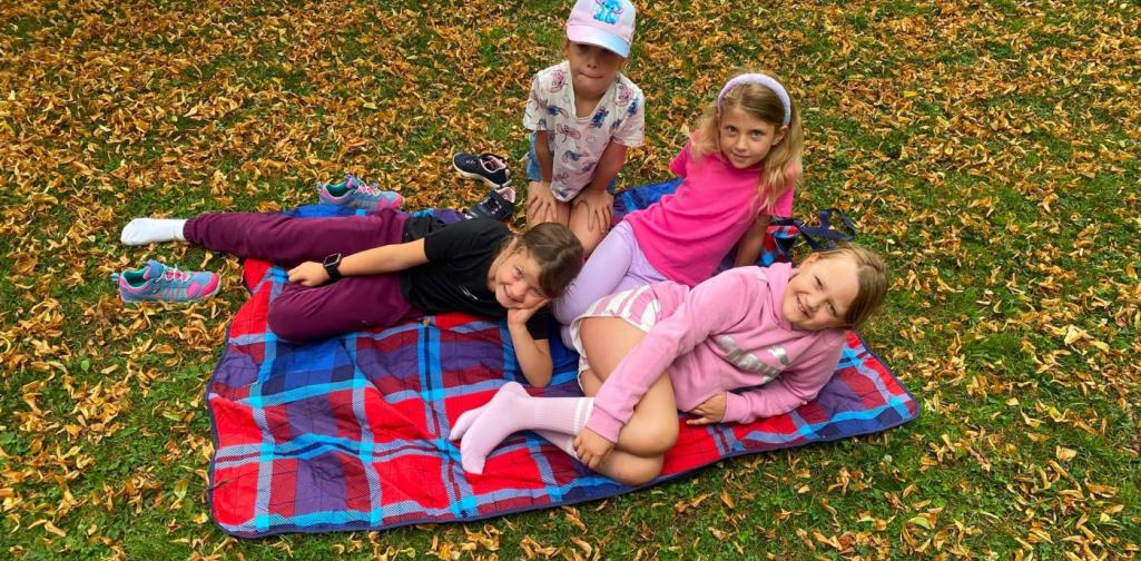 Vier Kinder entspannen gemeinsam auf einer Picknickdecke im Schlosspark und genießen ihre Pause.