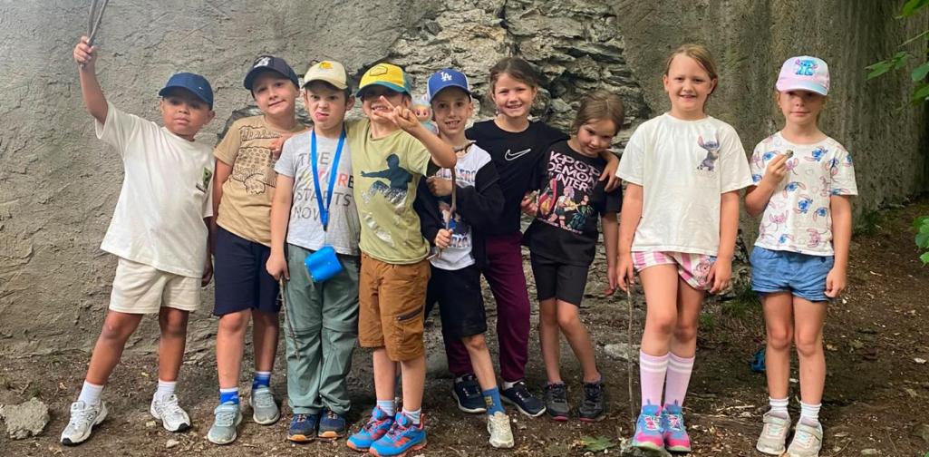 Eine Gruppe von Kindern erkundet gemeinsam den Schlosspark und posiert fröhlich vor einer alten Steinmauer.