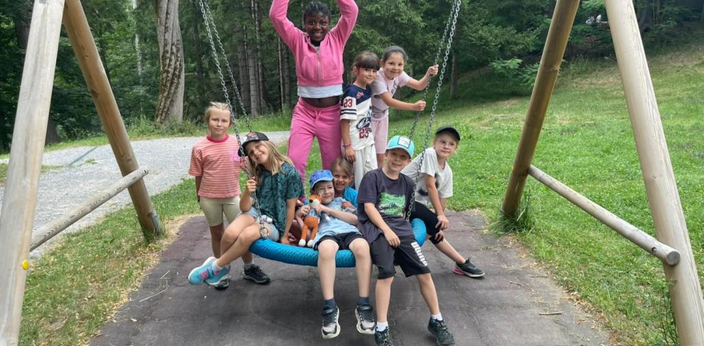 Kinder spielen gemeinsam auf einer Nestschaukel und haben sichtlich Spaß auf dem Spielplatz im Schlosspark.“