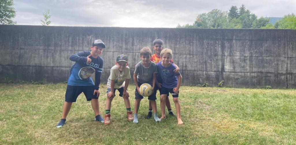 Fünf Kinder stehen mit einem Fußball auf einer Wiese im Schlosspark und posieren gemeinsam für ein Foto.