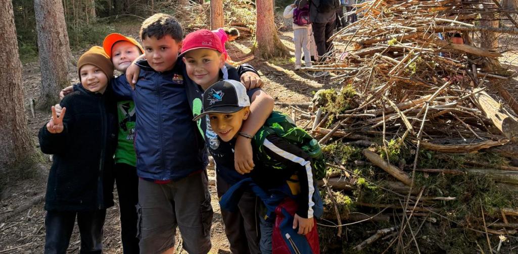 VS Amras Fünf Kinder stehen gemeinsam vor einem großen Stapel aus Ästen im Wald.