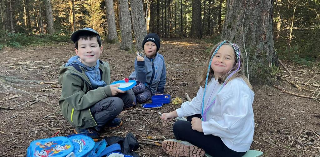 VS Amras Drei Kinder machen gemeinsam eine Jausenpause im Wald.