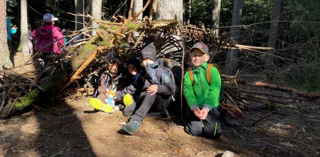VS Amras Vier Kinder sitzen in einem selbstgebauten Unterschlupf aus Ästen und Moos im Wald.