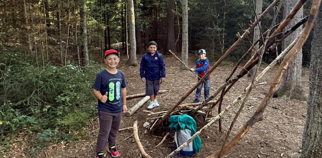 VS Amras Drei Kinder bauen im Wald gemeinsam einen Unterschlupf aus Ästen und Holz.