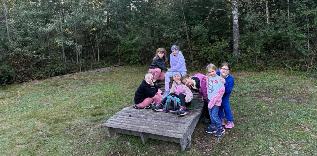 VS Amras Kinder sitzen und stehen gemeinsam auf einer Holzplattform am Waldrand.