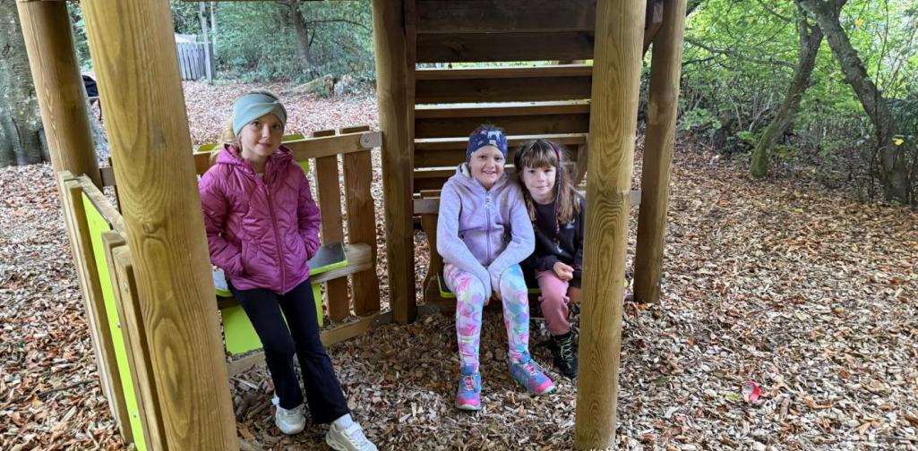 VS Amras Drei Kinder sitzen in einem Holzspielhaus auf einem Waldspielplatz.